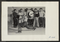[recto] An instructor in the weight lifting class at this relocation center demonstrates the proper handling of 200 pound bars to a group of aspiring students. ;  Photographer: Parker, Tom ;  Heart Mountain, Wyoming.