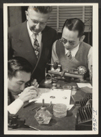[recto] Watch repairing is the vocation of Mr. Hajime Yenari (left). He is shown giving the detailed touches to a watch ...