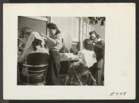 [recto] With makeshift equipment and arrangements, the cooperative beauty salon does a rushing business. ;  Photographer: Parker, Tom ;  Amache, Colorado.