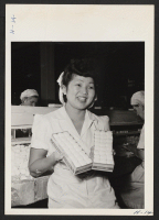 [recto] Miss Susie Yuasa, 18, a former evacuee from the Jerome Relocation Center, now employed in a Chicago candy factory, turns from her task momentarily to display the familiar symbol of victory. Susie's job is packaging marshmallows. ;  Photographer: Mace, C