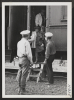 [recto] W.R.A. wardens, stationed at Tule Lake, help passengers to alight from the coaches on arrival at the Tule Lake station. ;  Photographer: Mace, Charles E. ; , .