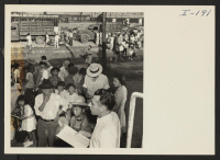 [recto] Closing of the Jerome Center, Denson, Arkansas. View from the train platform during loading of evacuees to the Gila River Center. A W.R.A. representative checks the list of passenger as they board the train from the trucks shown unloading in the backgroun