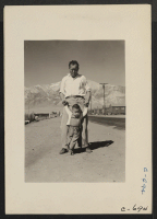 [recto] Manzanar, Calif.--Grandfather of Japanese ancestry teaching his little grandson to walk at this War Relocation Authority center for evacuees. ;  Photographer: Lange, Dorothea ;  Manzanar, California.