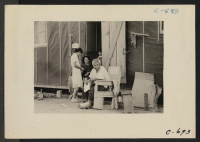 [recto] Manzanar, Calif.--Evacuee family of Japanese ancestry relax in front of their barrack room at the end of day. The father ...