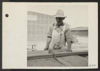 [recto] Japanese resident at the Topaz Center operating the power driven saw in preparing standard pieces for the interior construction of barracks. ;  Photographer: Parker, Tom ;  Topaz, Utah.