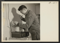 [recto] Takeshi Shindo, Manzanar Free Press reporter, tastes some home-cooked soup, prepared on the electric plate in his barracks home. ;  Photographer: Stewart, Francis ;  Manzanar, California.