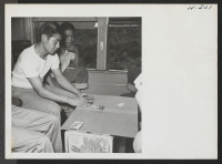 [recto] Passengers enroute to Tule Lake spend most of their time reading and sleeping. A few, however, played Japanese games. This traveler wiles away the hours with the good old American game of solitaire. ;  Photographer: Mace, Charles E. ; , .