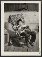[recto] Poston, Ariz.-- Robert Naeda, 9, son of the first family to arrive at this War Relocation Authority center, studies his school lessons in a home-made chair. His family are evacuees from El Centro, California. ;  Photographer: Stewart, Francis ;  Posto