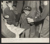 [recto] A soldier of the Army Transport Command hands a cup of milk to a small boy about to return to ...