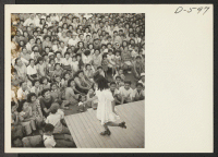 [recto] A young evacuee of Japanese ancestry entertains her fellow evacuees with a demonstration of her tap dancing ability. This was one number in an outdoor musical show. ;  Photographer: Stewart, Francis ;  Poston, Arizona.