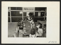[recto] Milk and graham crackers being served to nursery school children in a block recreation hall. The nursery teacher is Mrs. Sumi Kashiwagi. ;  Photographer: Parker, Tom ;  Amache, Colorado.