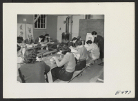 [recto] In an adult class, resident women are learning fine needle work and other crafts that will contribute to the comfort of their barracks homes. The teacher is (right) Mrs. A. Akuda. ;  Photographer: Parker, Tom ;  Amache, Colorado.