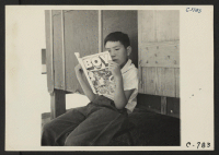 [recto] Manzanar, Calif.--Evacuee boy at this War Relocation Authority center reading the Funnies. ;  Photographer: Lange, Dorothea ;  Manzanar, California.