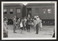 [recto] INCOMING--Arrivals leaving train assisted by Girl Scout with their baggage. ;  Photographer: Aoyama, Bud ;  Heart Mountain, Wyoming.