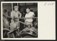 [recto] Archie Wiels, engineer at the Becker Cold Storage Plant, confers with Paul Shimada, Labor Supervisor, in the refrigeration room. Mr. Shimada is formerly from the Rohwer Relocation Center and Lodi, California. ;  Photographer: Iwasaki, Hikaru ;  Decatu