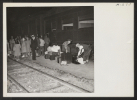 [recto] Transferees arriving from Tule Lake on trip 14 await the arrival of a bus to take them to their new quarters, while wardens gather up their hand luggage. ;  Photographer: Mace, Charles E. ;  Topaz, Utah.