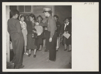 [recto] One of the many wardens on duty at the Tule Lake induction center directs new arrivals from Topaz to the photographic department, where they will have their identification pictures taken and also be finger printed. ;  Photographer: Mace, Charles E. ;