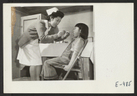 [recto] The school administers a throat swabbing to a young grade school student. One room of the school barracks block is occupied by the school nursing staff, who maintain careful watch and administer, under the hospital doctor, ordinary medical treatment. ;