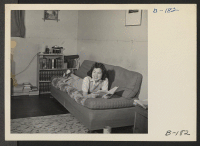 [recto] Lucy Yonemitshu, former student from Los Angeles, California, enjoys a pleasant moment with her book. Lucy lives with her parents in this barrack home, which has been very tastefully decorated by her father. ;  Photographer: Stewart, Francis ;  Manzan