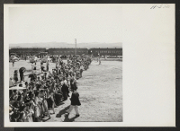 [recto] Residents of the Heart Mountain Relocation Center wait along the barrier to greet long separated friends and relatives arriving on trip 24 from Tule Lake. ;  Photographer: Mace, Charles E. ; , .