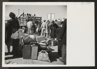 [recto] New residents at Heart Mountain who arrived on trip 24 from Tule Lake wait with their hand luggage to be conveyed to their new quarters. ;  Photographer: Mace, Charles E. ; , .