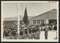 [recto] Amache Boy Scouts raising flag to half-mast at Memorial Service for first six Nisei soldiers from this Center killed in action in Italy. The service was held August 5, 1944, and attended by 1500 Amache residents. ;  Photographer: McClelland, Joe ;  Am