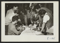 [recto] A group of volunteer beet workers look over the labor contracts which will provide their unit with seasonal work outside the relocation center and assist the farmers in harvesting the all important beet sugar crops of 1942. ;  Photographer: Parker, Tom