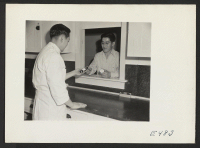 [recto] A resident of the center receives a prescription over the counter of the prescription laboratory. Three licensed pharmacists are on duty at the pharmacy. ;  Photographer: Parker, Tom ;  Amache, Colorado.