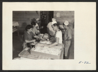 [recto] Kitchen crews preparing pork chops for the evening meal of the first volunteer worker arrivals at the relocation center. Former residence: Merced Assembly Center, Merced, California. ;  Photographer: Parker, Tom ;  Amache, Colorado.