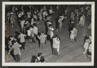 [recto] Dancing is one of the chief forms of recreation at the Heart Mountain Relocation Center. This scene in the High School Gymnasium shows the portion of the crowd at a school dance to which the public was invited. ;  Photographer: Iwasaki, Hikaru ;  Hear