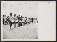 [recto] Boys Drum Corps at Tule Lake plays at the center's gateway, as buses, laden with evacuees being transferred to Tule Lake, pass through on their way to the train at Delta, Utah. ;  Photographer: Mace, Charles E. ;  Topaz, Utah.