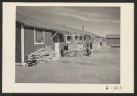 [recto] A typical barracks building. The weather canopies over the doors were constructed by the residents. The bicycle is a rare article in the center, and its owner is indeed fortunate. ;  Photographer: Parker, Tom ;  Amache, Colorado.