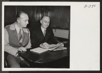 [recto] Morlin Kurtz, representing W.R.A. in the movement of transferees between Heart Mountain and Tule Lake, confers with F. L., Cobb, District Passenger Agent for the Great Northern Railway, aboard the train on trip 24. ;  Photographer: Mace, Charles E. ;