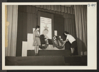 [recto] Memorial Services were held for the six war dead. The girl, pictured at the left, is a Girl Scout, while a Camp Fire Girl is laying a wreath before the community gold star service flag. ;  Photographer: Ushioka, Henry ;  Heart Mountain, Wyoming.