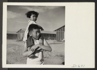 [recto] Parker, Arizona --A little evacuee of Japanese ancestry gets a ride on her brother's shoulders at this War Relocation Authority center where they are spending the duration. ;  Photographer: Stewart, Francis ;  Poston, Arizona.