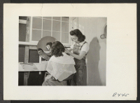 [recto] With makeshift equipment and arrangements, the cooperative beauty salon does a rushing business. ;  Photographer: Parker, Tom ;  Amache, Colorado.