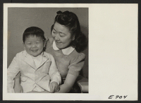 [recto] Kay Kawahara, three year old son of Dr. Kazuto Kawahara, a former Los Angeles dentist, being held by a neighbor Joan Ishiyama. Joan is a stenographer in the office of the Project Director, Guy Robertson. ;  Photographer: Parker, Tom ;  Heart Mountain,