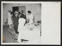 [recto] Doctors and nurses, in the induction center at Topaz, examine the new arrivals from Tule Lake before they are assigned to their new quarters. ;  Photographer: Mace, Charles E. ;  Topaz, Utah.