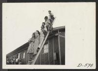 [recto] Evacuees of Japanese descent on odd perch watching an outdoor musical performance at this War Relocation Authority center for evacuees of Japanese ancestry, where they are spending the duration. ;  Photographer: Stewart, Francis ;  Poston, Arizona.