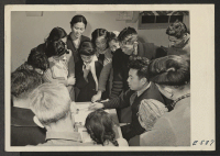 [recto] In a night school art class at the Heart Mountain Relocation Center, students gather around the instructor for criticism. Classes ...