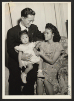 [recto] Former S/Sgt. Henry H. Gosho is shown with his wife and 18-month-old daughter Carol Jeanne preceding a dinner in his ...