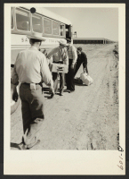 [recto] Unloading baggage belonging to evacuees of Japanese ancestry. Caucasian construction employees assist evacuees in getting their belongings from the bus at the relocation center. ;  Photographer: Clark, Fred ;  Poston, Arizona.