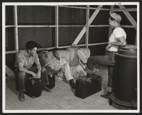 [recto] Three young evacuees drop their baggage and relax to argue about whose bunk goes in which corner on arriving at their new quarters. ;  Photographer: Parker, Tom ;  Amache, Colorado.