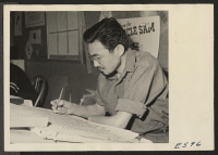 [recto] A young Nisei artist works on a lettering design for a poster to be used as part of a rubber saving drive at the Heart Mountain Relocation Center. ;  Photographer: Parker, Tom ;  Heart Mountain, Wyoming.