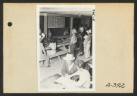 [recto] Poston, Ariz.--Evacuees of Japanese [ancestry] registering at this War Relocation Authority. The sign explains features of WRA work corps. ;  Photographer: Clark, Fred ;  Poston, Arizona.