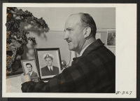[recto] Charles F. Ernst, Project Director, is shown with photographs of his two sons, who are now in the armed services. ;  Photographer: Stewart, Francis ;  Topaz, Utah.