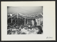 [recto] Since there are no movies, talent shows are extremely popular at the center, and this mess hall, converted for an evening's block talent show, is crammed to capacity with other residents crowding for window space on the outside. ;  Photographer: Parker,