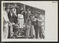 [recto] A group of students gathers around the entrance to the principal's office with Ralph Forsythe, assistant principal. ;  Photographer: Hosokawa, Bill ;  Heart Mountain, Wyoming.