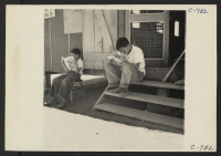 [recto] Manzanar, Calif.--Evacuee boys of Japanese ancestry at entrance of Recreational Hall reading Funnies. ;  Photographer: Lange, Dorothea ;  Manzanar, California.