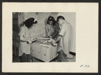 [recto] A part of the kitchen crew of the first arrival slices bacon for the first barracks breakfast to be served at this relocation center. Former residence: Merced Assembly Center, Merced, California. ;  Photographer: Parker, Tom ;  Amache, Colorado.